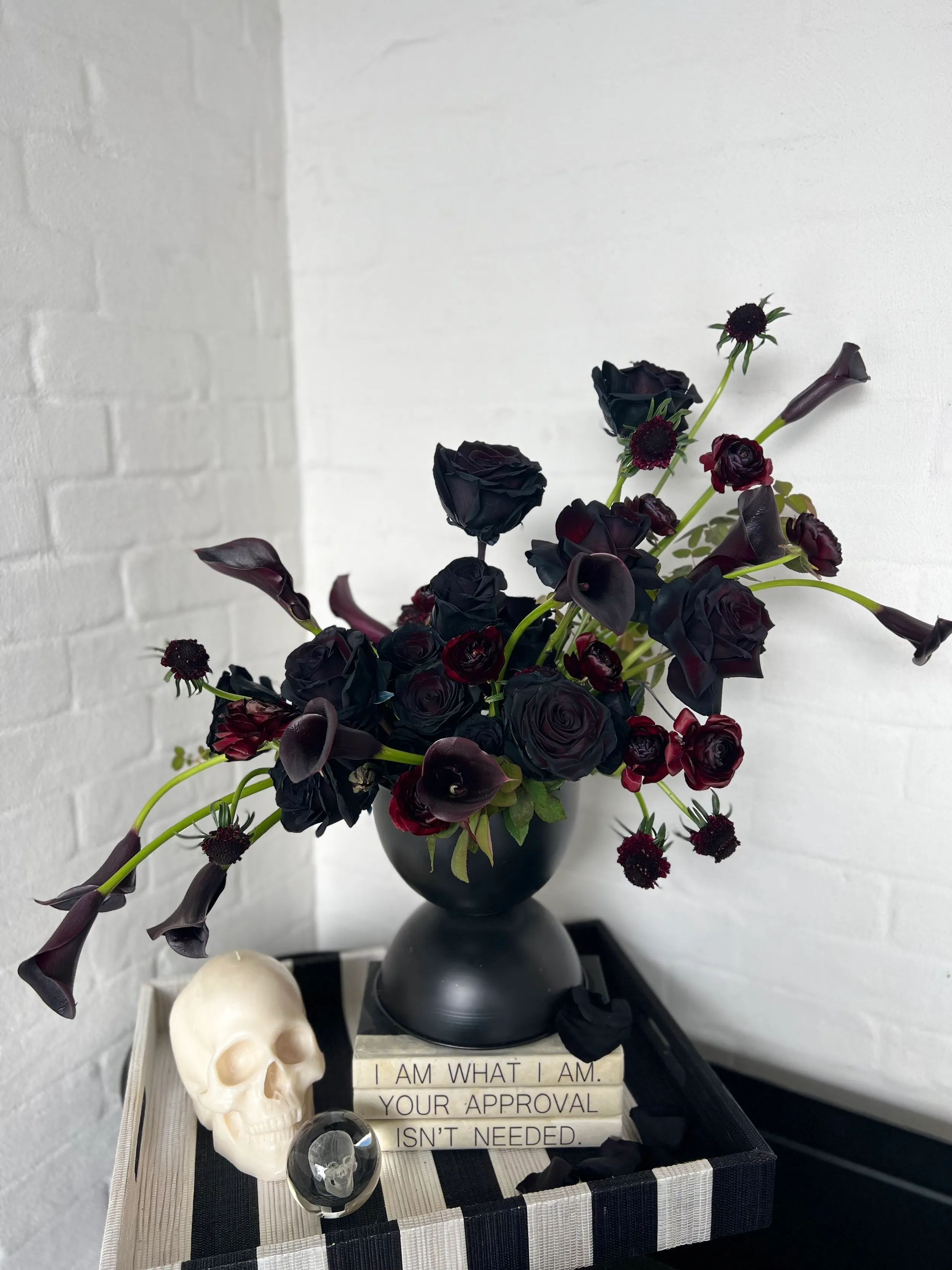 Dramatic dark floral arrangement of deep burgundy ranunculus and black calla lilies in a black urn.