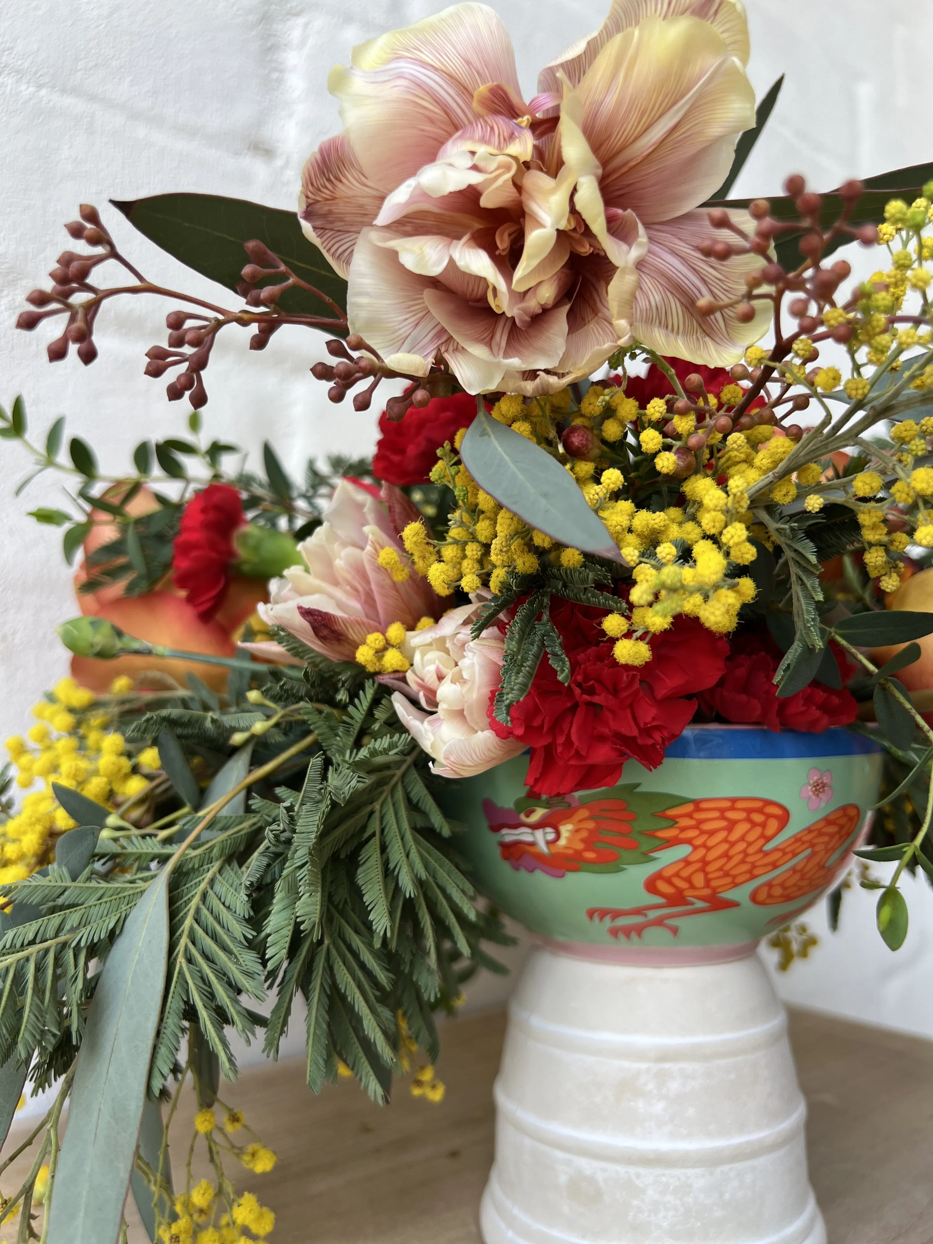 Crimson hydrangea, garden roses and plum calla lilies arranged low on a white pedestal against concrete.