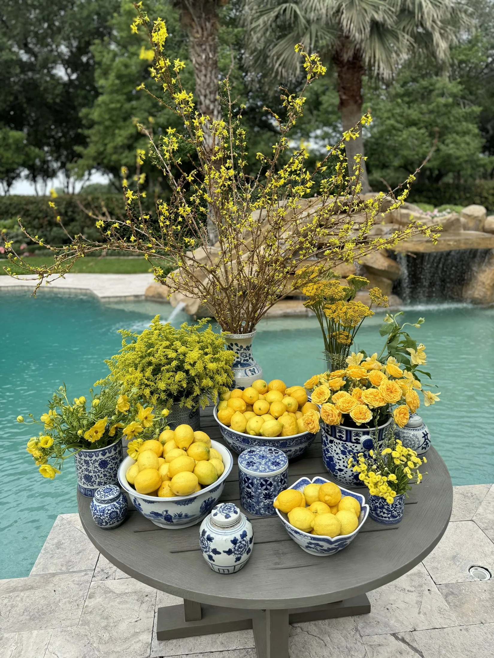 Forsythia, mimosa and bowls of lemons styled poolside on a stone table.
