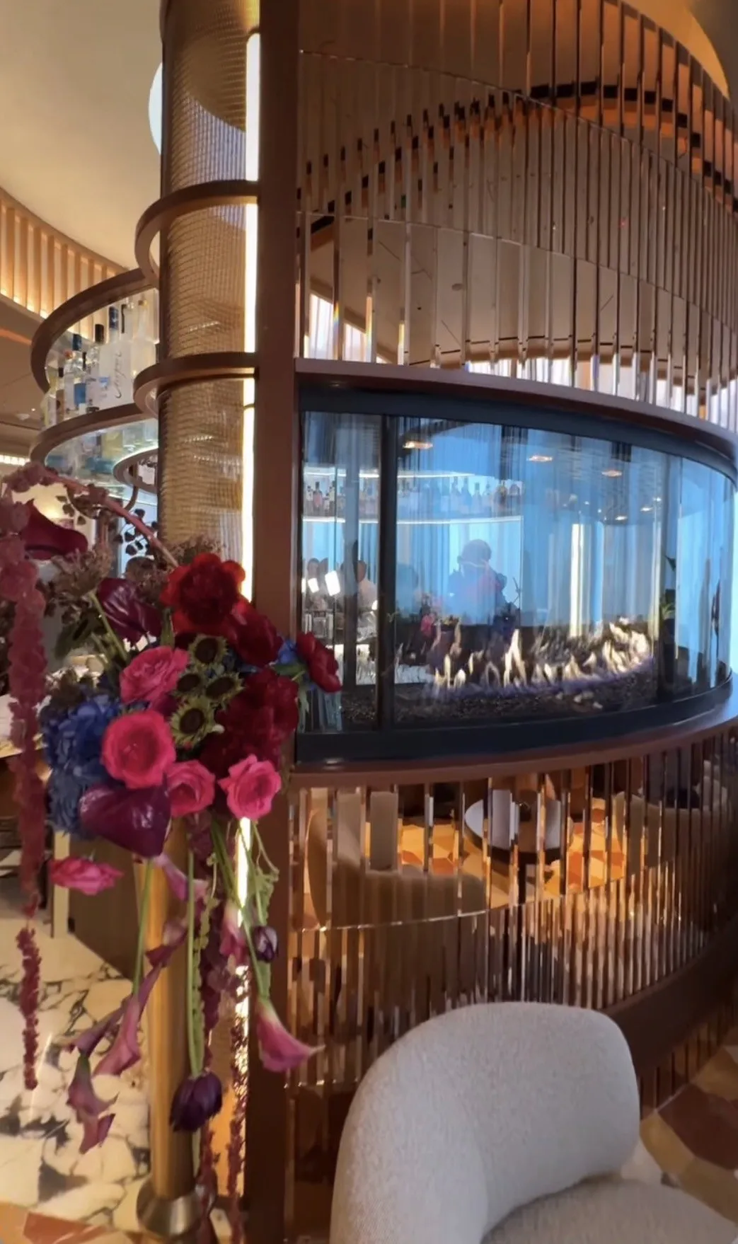 Jewel-tone florals in brass vessels beside a curved restaurant banquette.