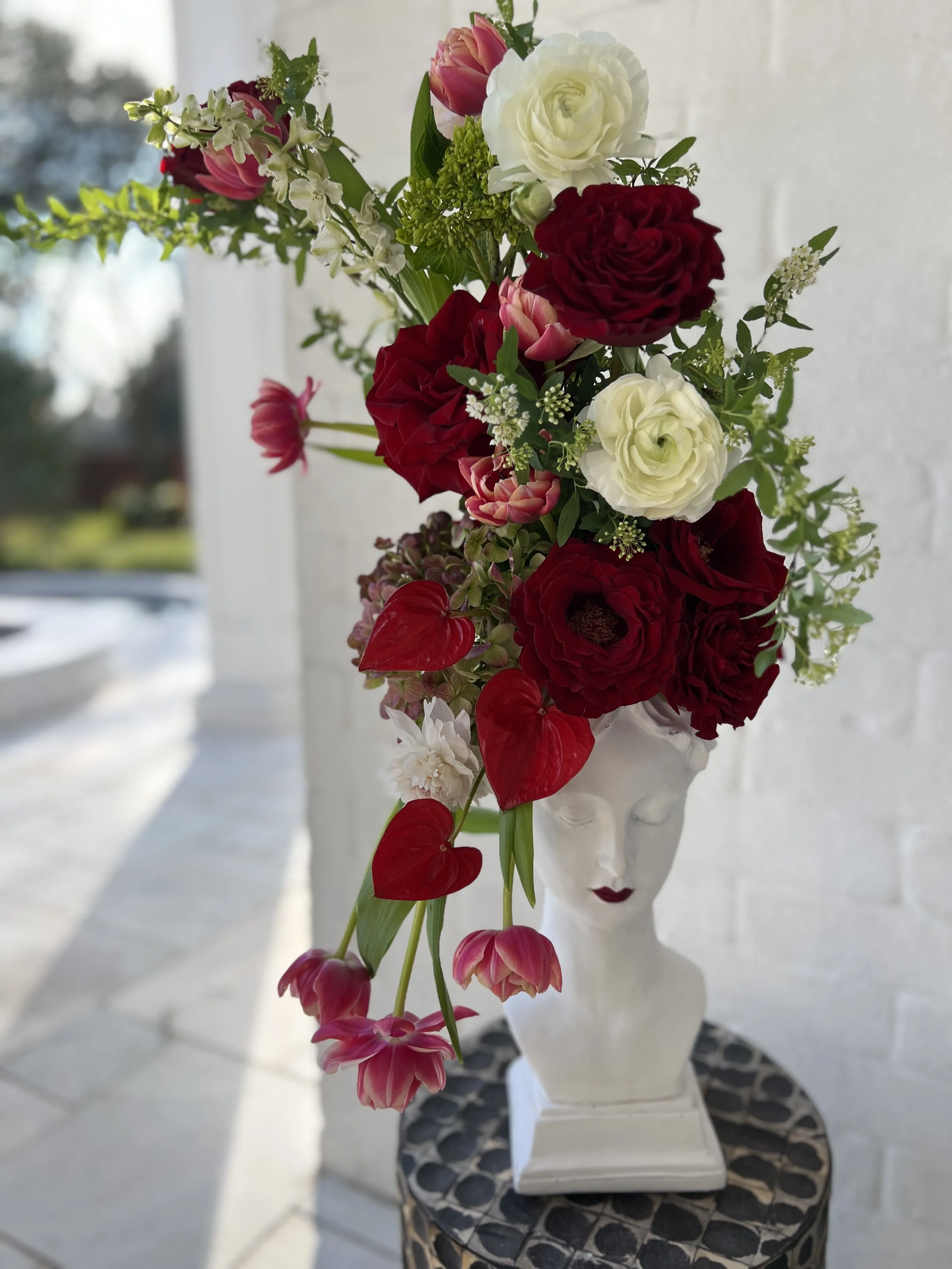 Classical bust crowned with red and white florals on a marble console.