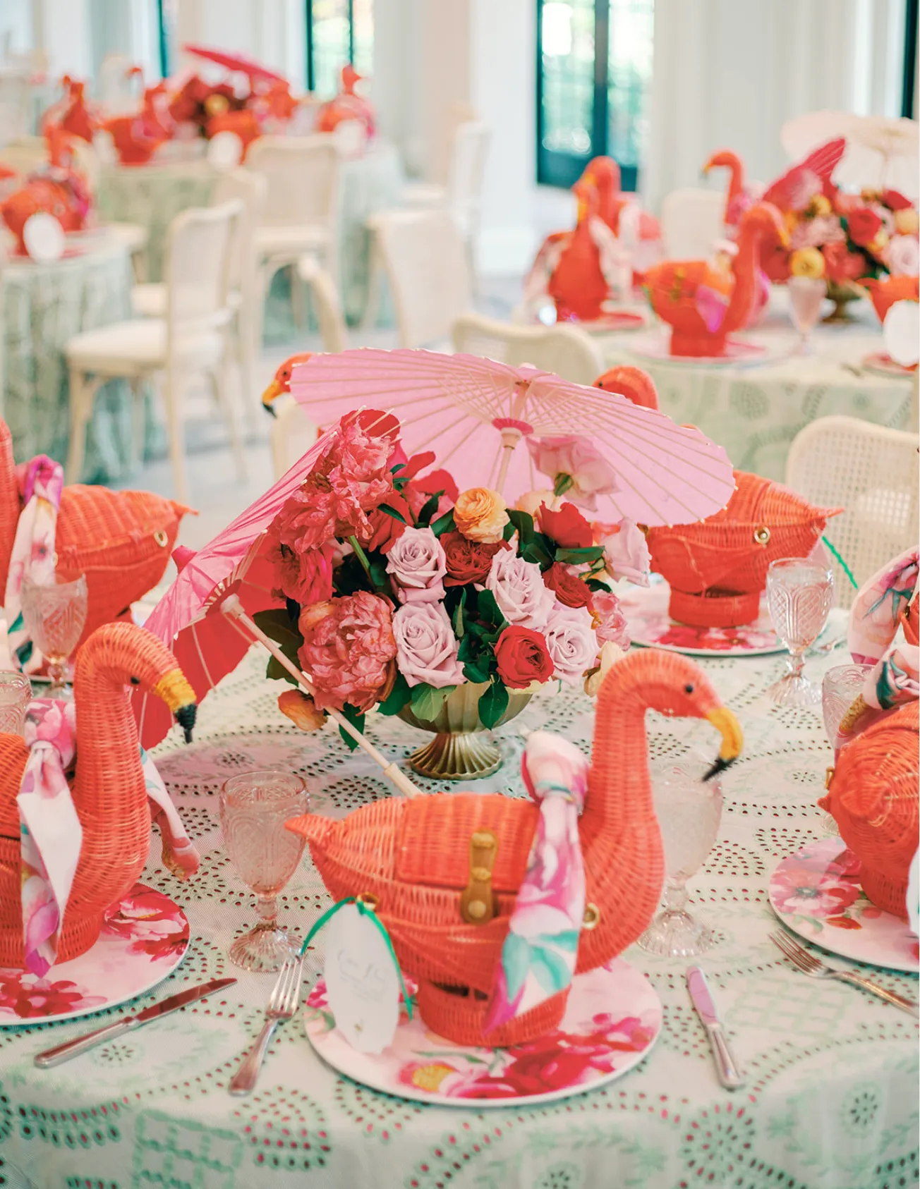 Tablescape of coral wicker flamingo baskets, parasols and roses on eyelet linen.