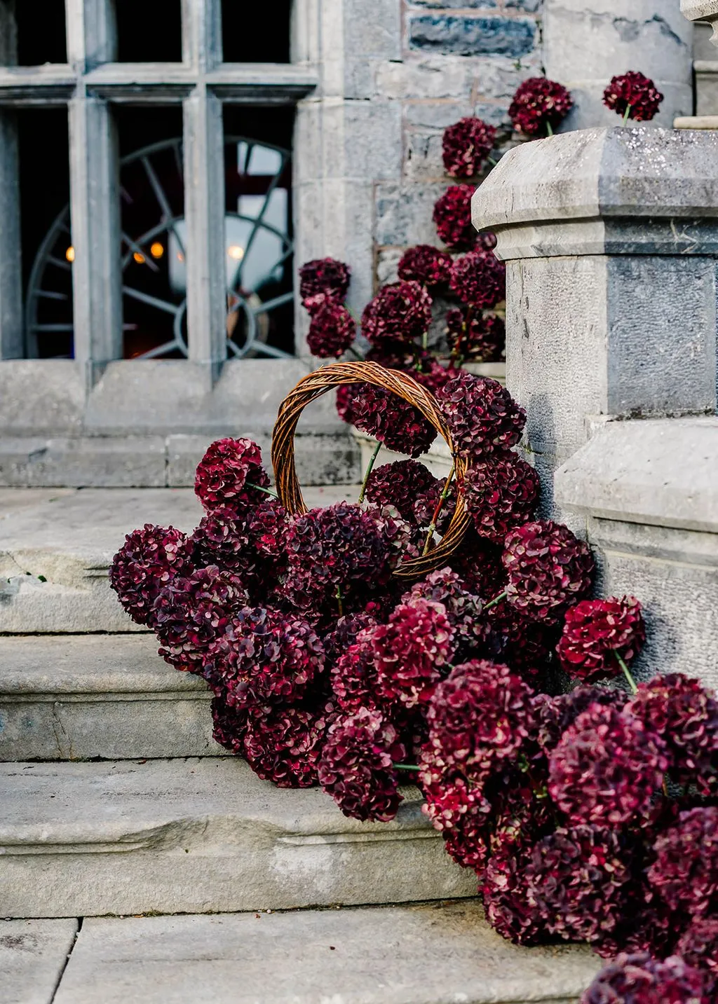 Deep burgundy hydrangeas spilling down stone castle steps with a willow basket.