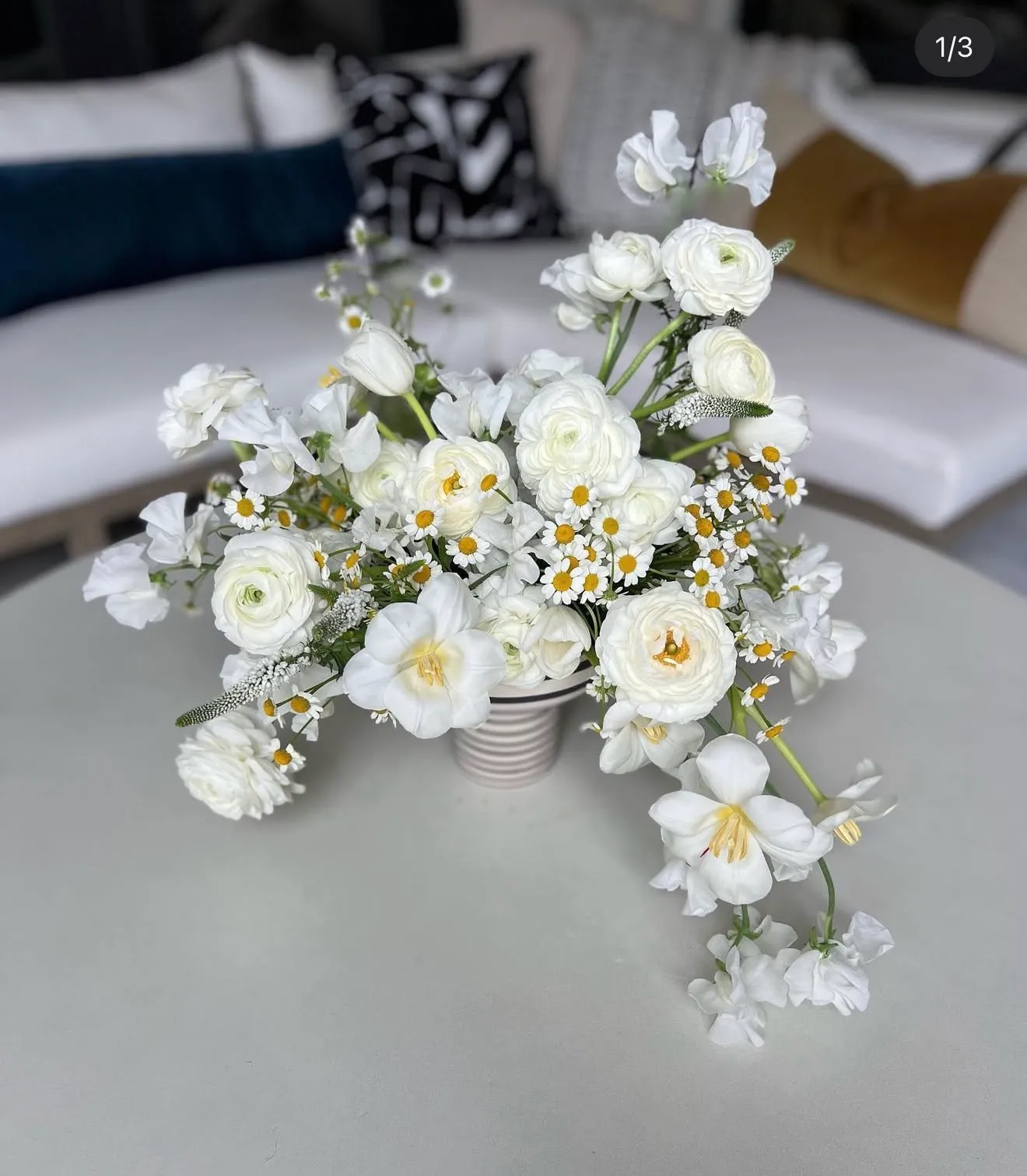 White ranunculus, chamomile and sweet peas in a ribbed vase on a round table.
