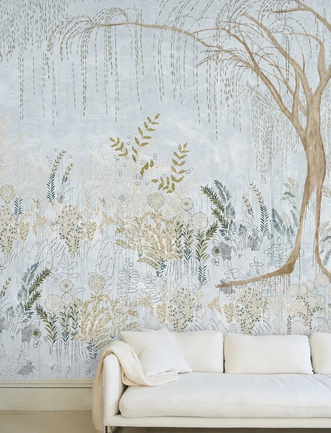 Hand-painted willow and wildflower mural in powder blue behind a white linen sofa.