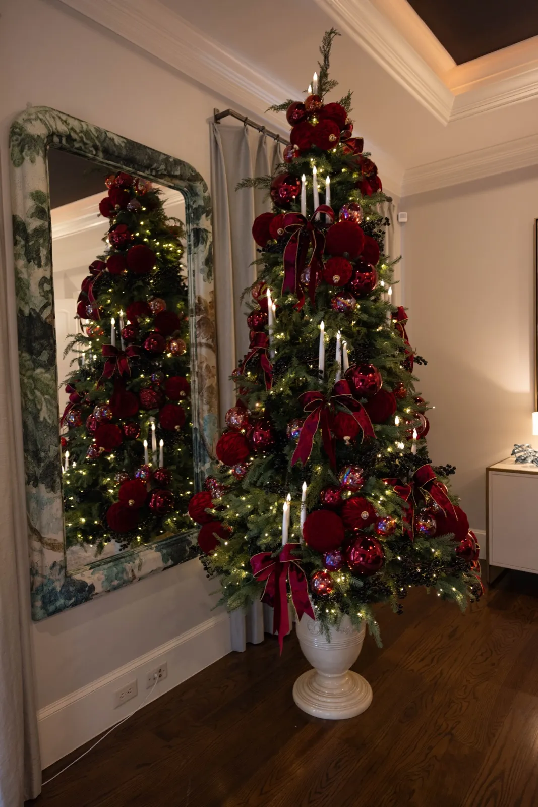 Burgundy-toned Christmas tree in an urn reflected in a tall mirror.
