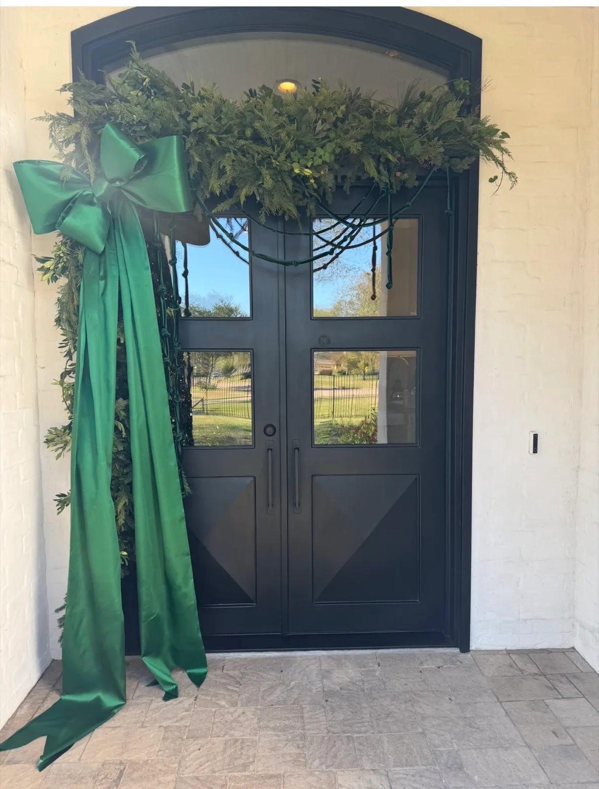 Iron double doors crowned with fresh garland and an oversized green velvet bow.