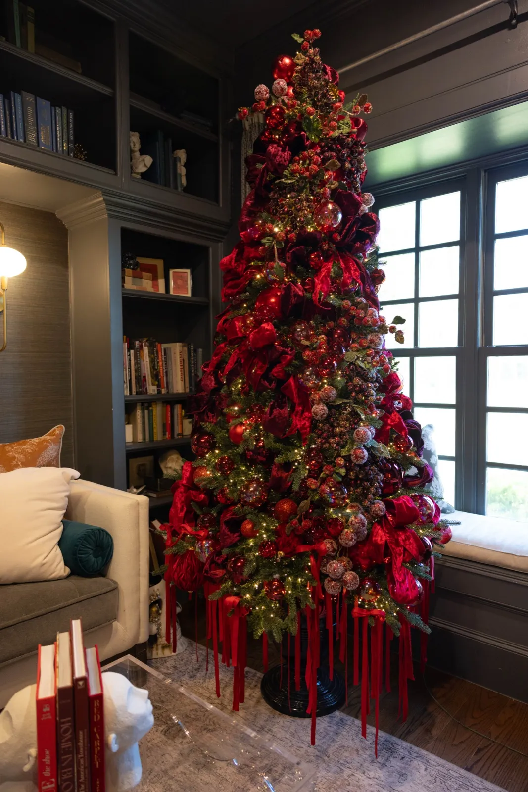 Deep red Christmas tree with trailing ribbon in a dark-paneled library.