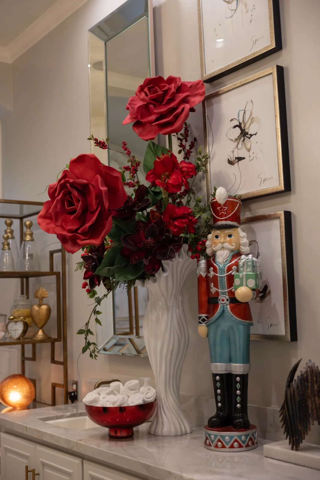 Oversized red roses and berries in a white vase beside a blue nutcracker.