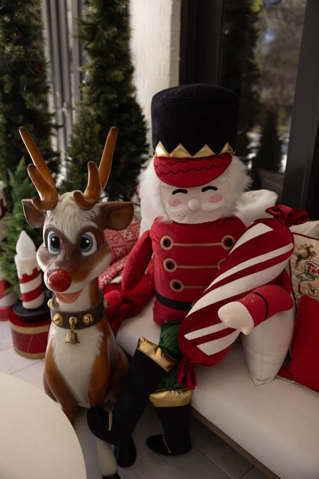 Rudolph and toy-soldier nutcracker figures with a candy cane on a white bench.