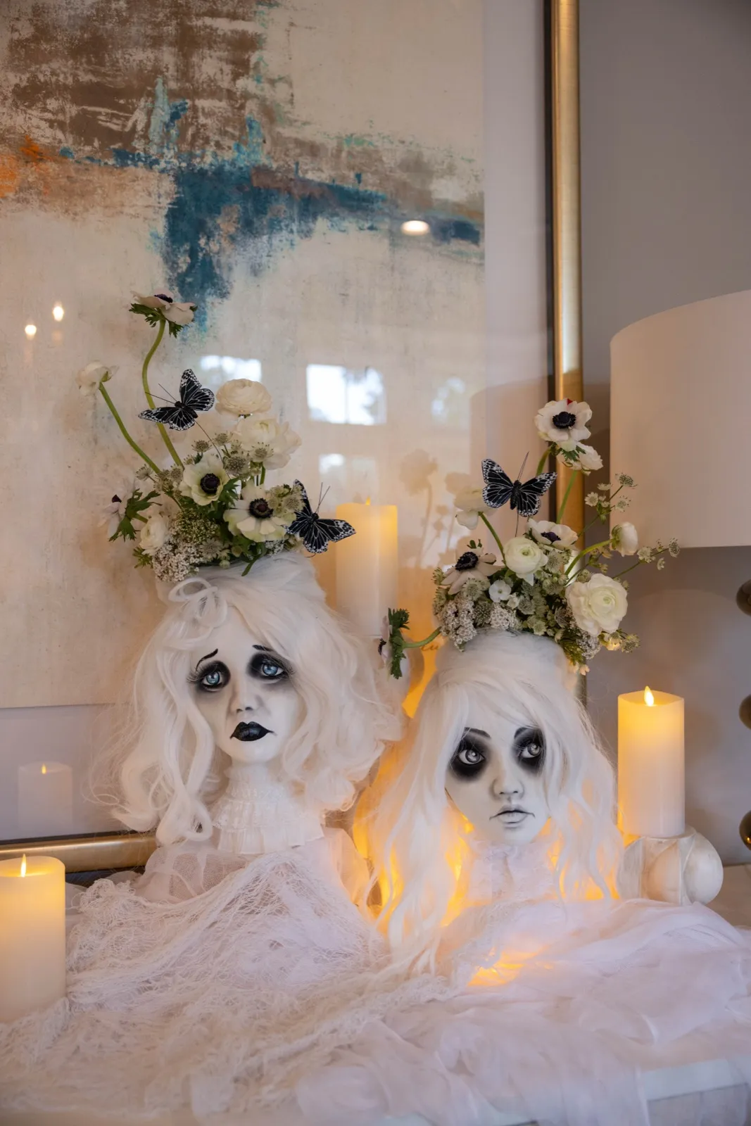 Ghostly white busts with anemones and pillar candles styled on a console beneath abstract art.