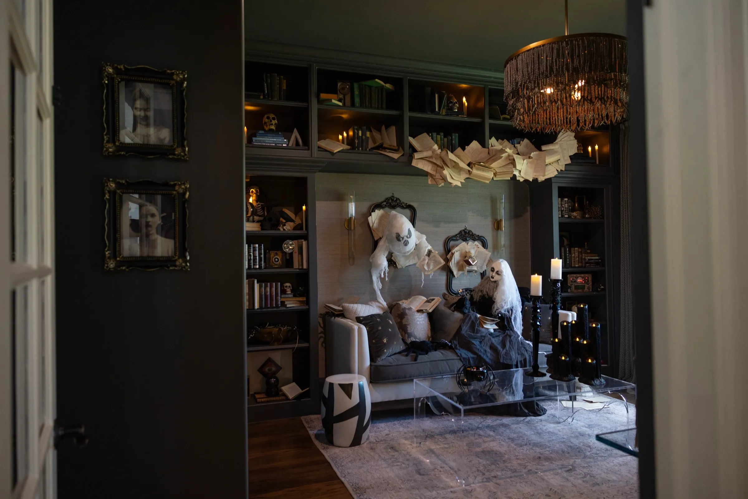 Moody library styled for Halloween: ghostly figures reading on the sofa beneath a flight of book pages.