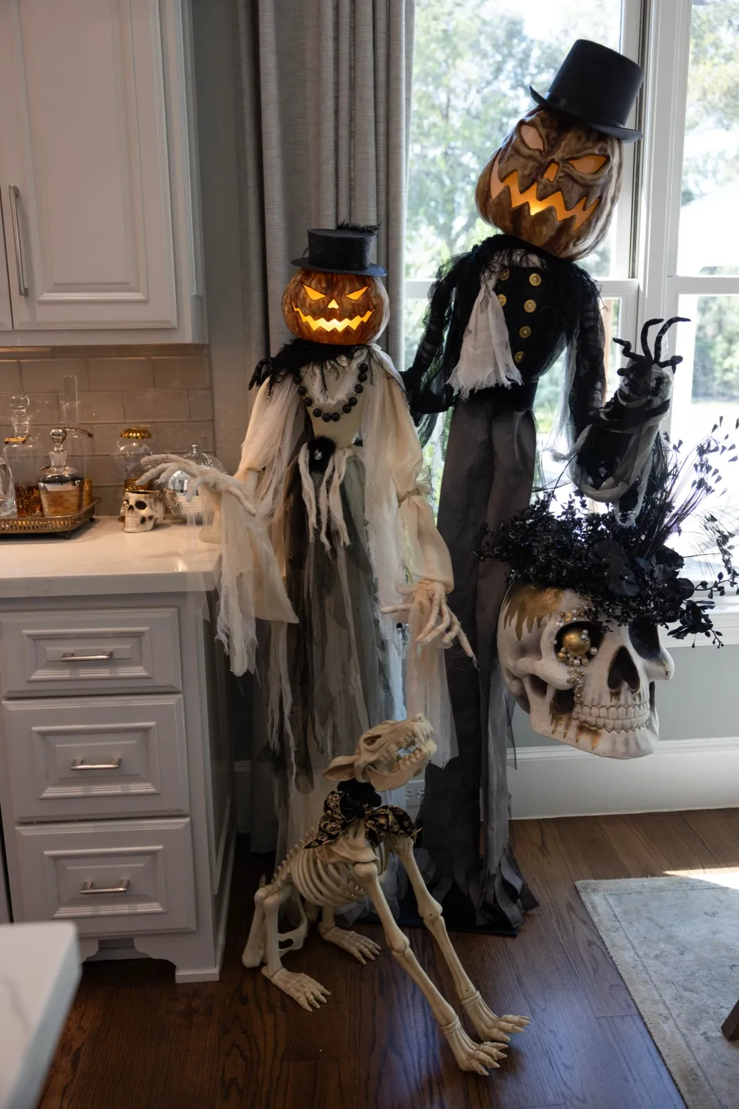 Top-hatted pumpkin-head figures and a skeleton dog styled in a white kitchen.