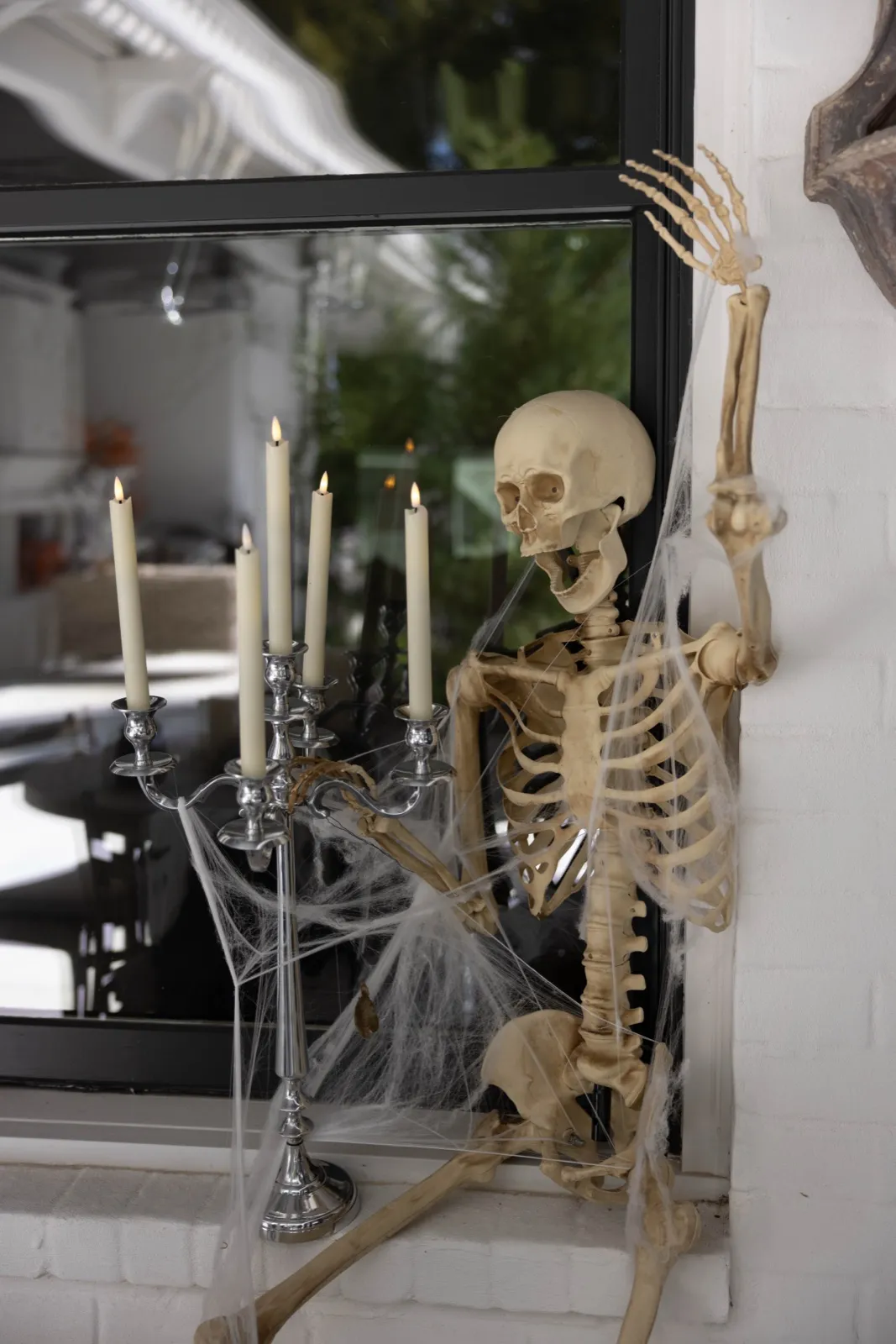 Skeleton climbing through a window beside a silver candelabra wrapped in cobwebs.