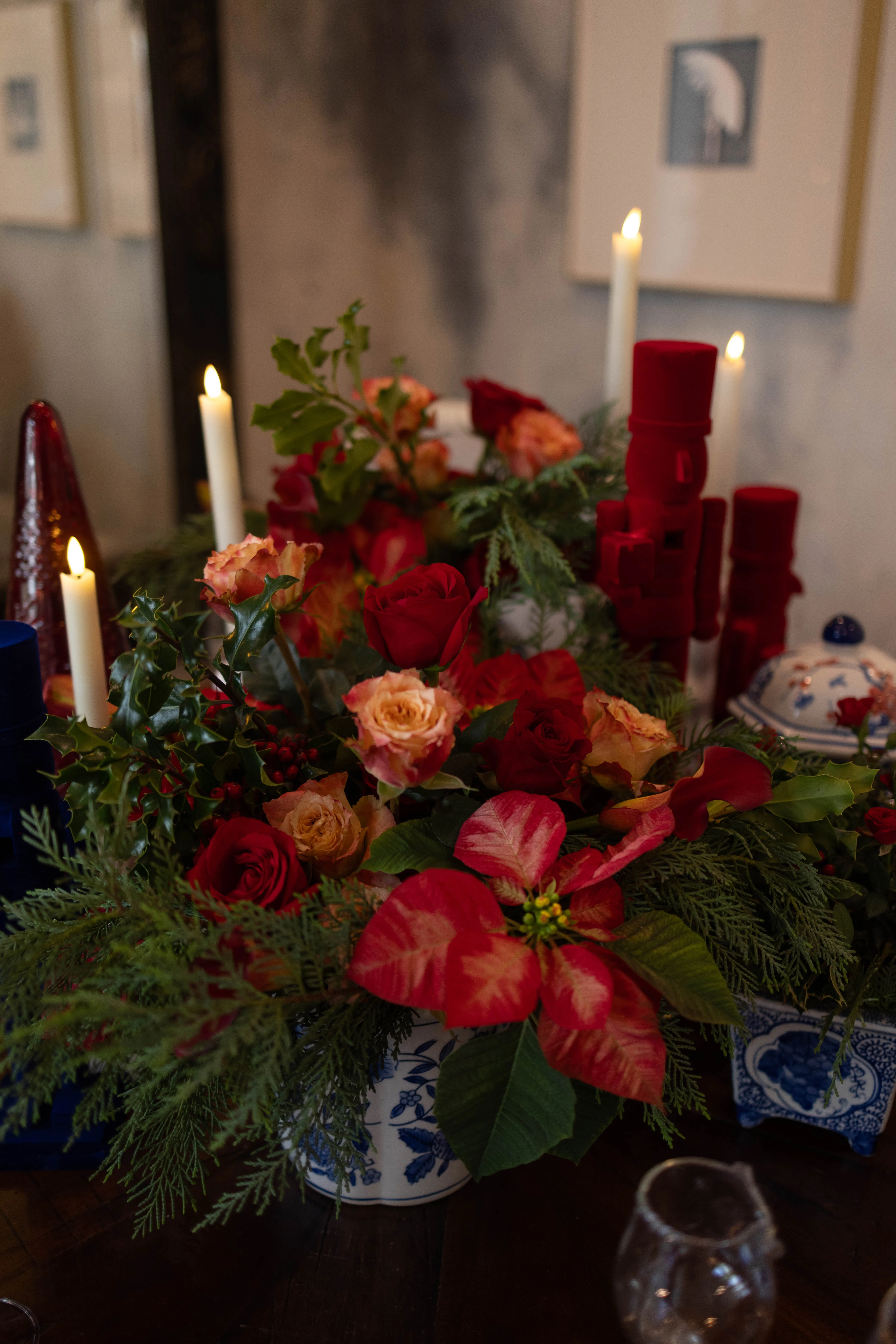 Candlelit holiday tablescape of red roses, poinsettias and pine in blue-and-white porcelain.